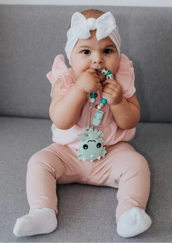 Rózsaszín ruhás kisbaba névre szóló rágcsalánccal ül a kanapén – Baby Panda